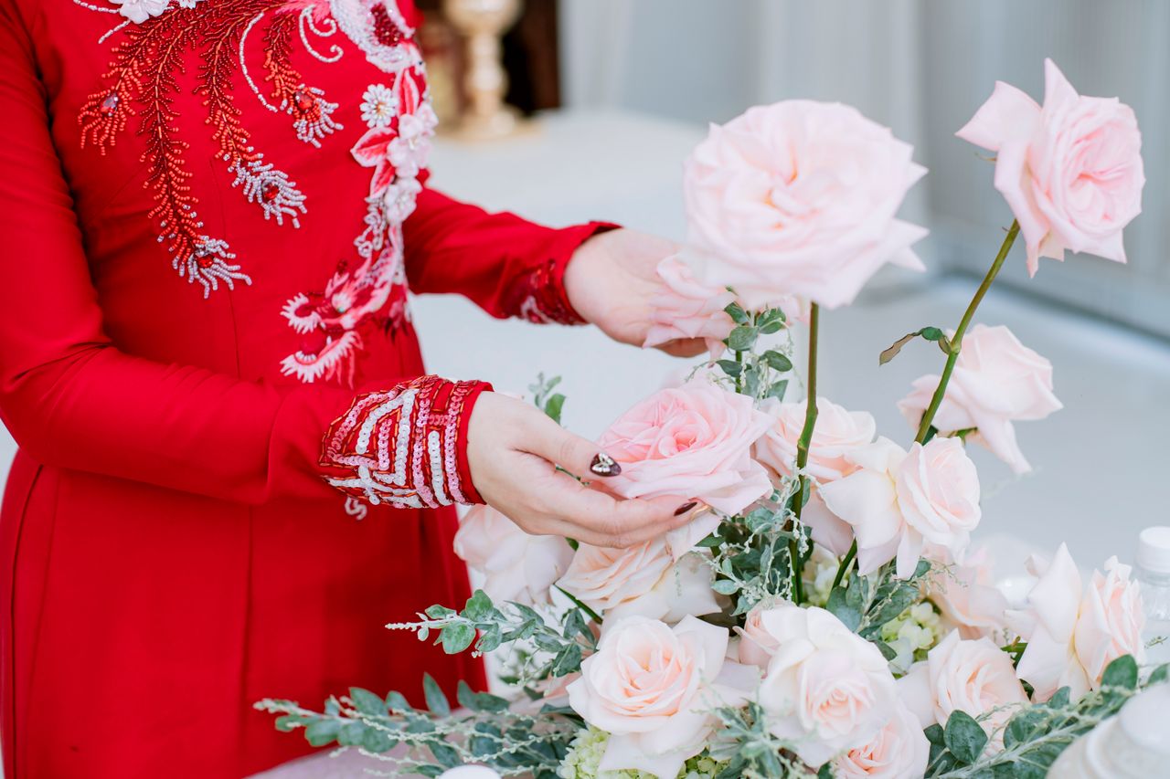 Close-up of pink roses with a woman's hands in an embroidered red dress, highlighting wedding details.